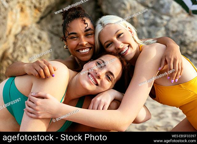 Happy multiracial friends leaning on each other at beach