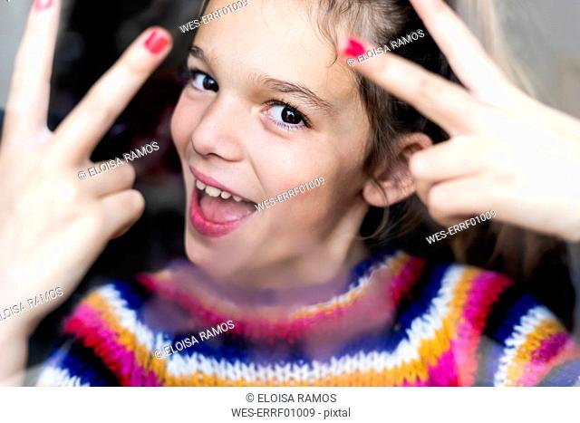 Portrait of happy playful girl in striped pullover behind windowpane