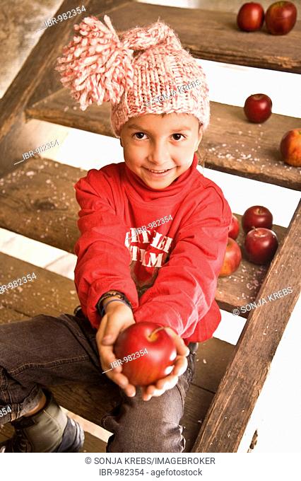 A boy is sitting on the stairs of a cottage and is holding an apple in his hand