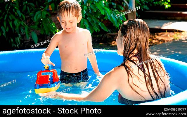 Cute little boy with young mother playing in swimming pool with toy ship or boat. Concept of happy and cheerful family summer holidays and vacation
