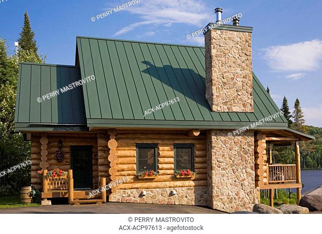 Handcrafted spruce log home facade with fieldstone chimney and green metal roof in summer, Quebec, Canada. This image is property released. CUPR0280