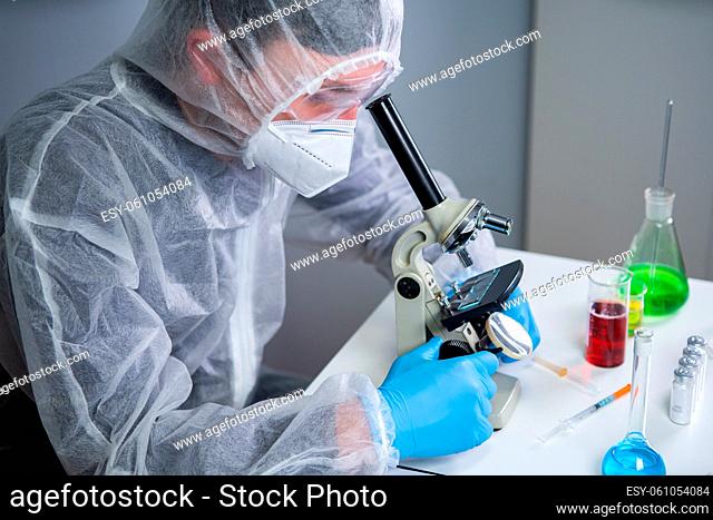 Scientist examining sample with a microscope, doing medical research in science laboratory. Male laboratory assistant in protective clothing studying new...