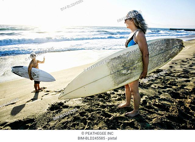 Older Caucasian couple standing on beach with surfboards