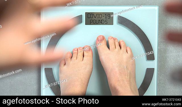 Feet standing on digital weight scale with the words COVID-19 Pounds written on, coronavirus and diet concept. top view crisis