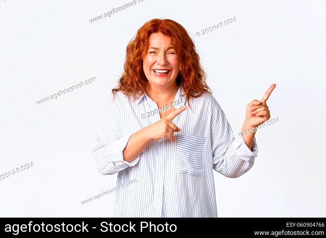 Happy gorgeous redhead woman, middle-aged lady laughing over something funny, chuckling and pointing fingers upper right corner, showing banner