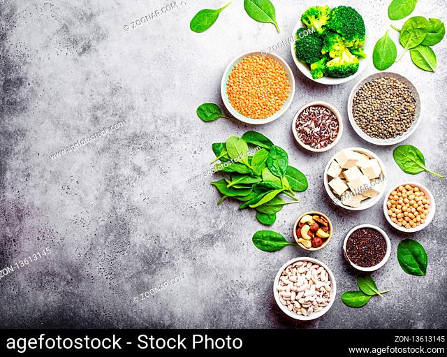 Top view of different vegan protein sources with space for text: beans, lentils, quinoa, tofu, vegetables, nuts, chickpeas, rice, stone background