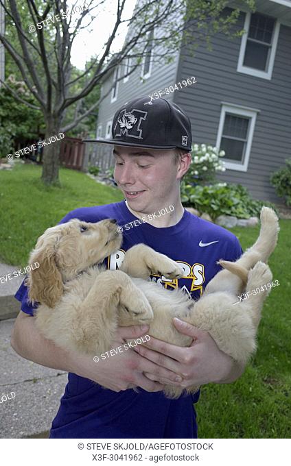 My teenage grandson holding Odin, his new Goldendoodle puppy in front of his home. St Paul Minnesota MN USA