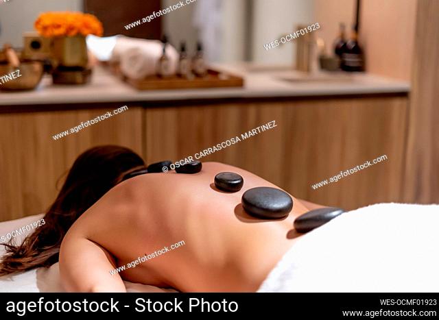 Young woman lying with stones on her back during lastone therapy at health spa