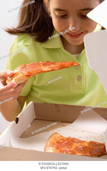 Little girl holding slice of pizza over pizza box