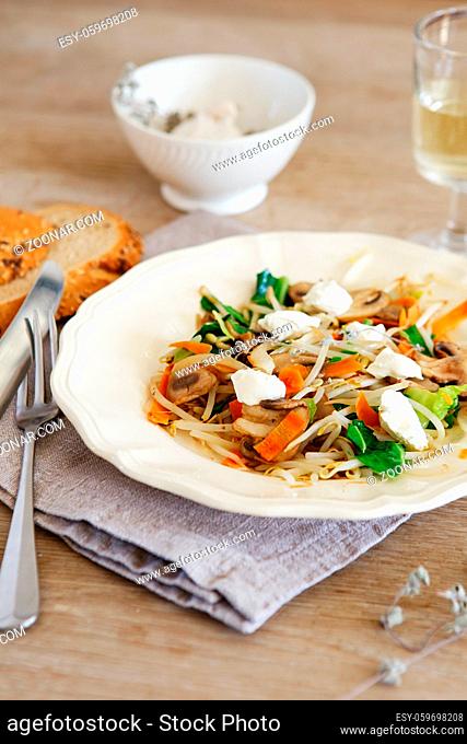 Mixed vegetable stir fry with mushrooms and cottage cream cheese. Tender mushroom stir fry served in a white plate with white wine and bread on the wooden table