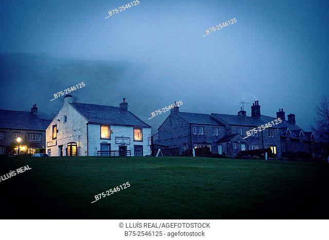 View of a village cottages with lights on in the windows and smoke in the chimneys on a cold winter day at dusk. Buckden, Yorkshire Dales, Skipton, England, UK