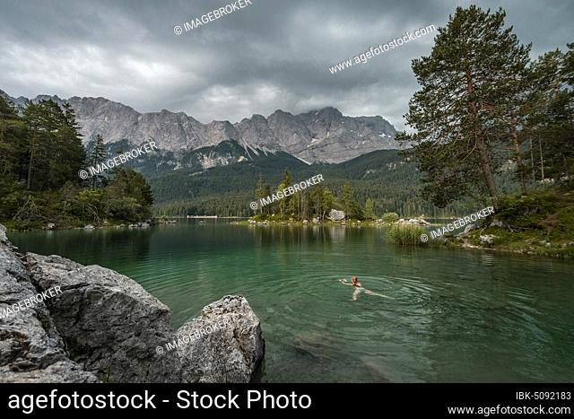 Woman swimming in the lake, rocks on the shore, view into the distance, Eibsee lake in front of Zugspitze massif with Zugspitze, Wetterstein range, near Grainau