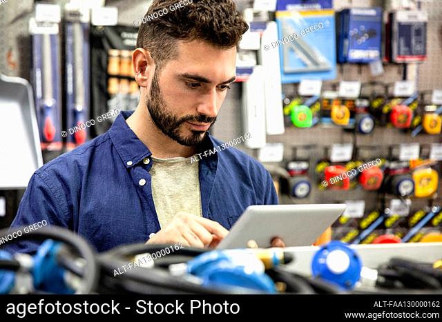 Male hardware shop owner taking inventory on digital tablet