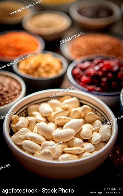 Raw white bean in ceramic bowl. Composition of superfoods in background. Placed on dark rusty table. Selective focus