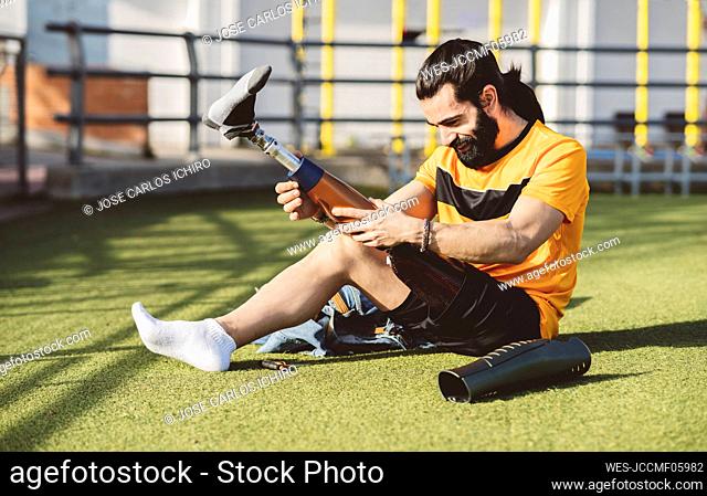 Smiling athlete wearing prosthetic leg sitting on grass