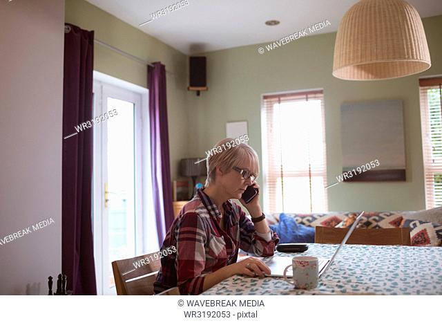 Mature woman talking on mobile phone while using laptop