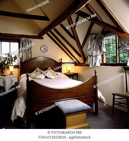 Antique mahogany bed with attic bedroom with small windows and beamed ceiling