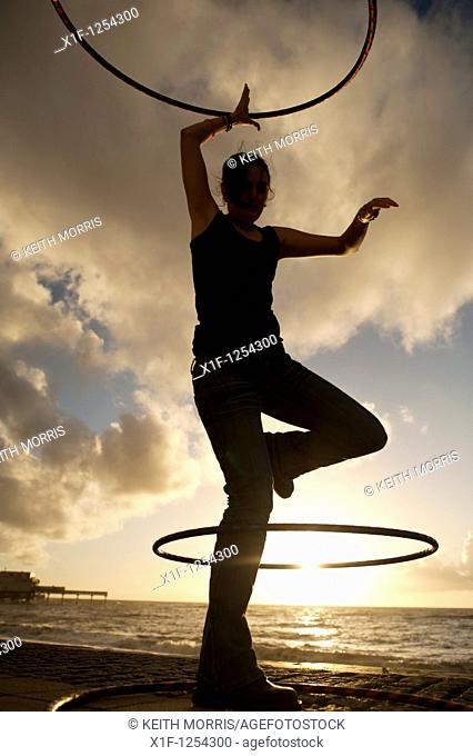 A young woman student at Aberystwyth university using hoolah hoops at sunset, UK