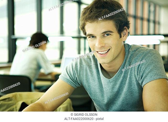Young man in university library, smiling at camera