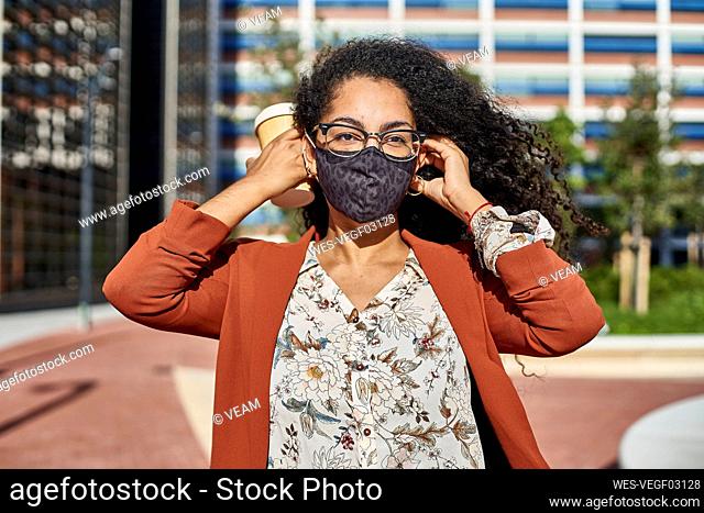 Young woman wearing protective face mask standing in city on sunny day