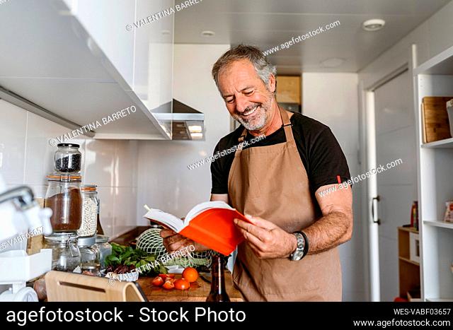 Mature man smiling while reading book in kitchen at home