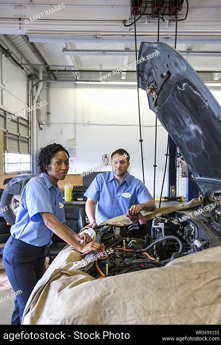Male and female mechanics talk as they look at engine in auto repair shop