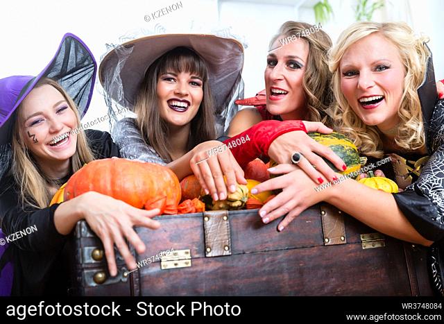 Portrait of four young and beautiful women wearing witch costumes while posing together with pumpkins and an old trunk at Halloween