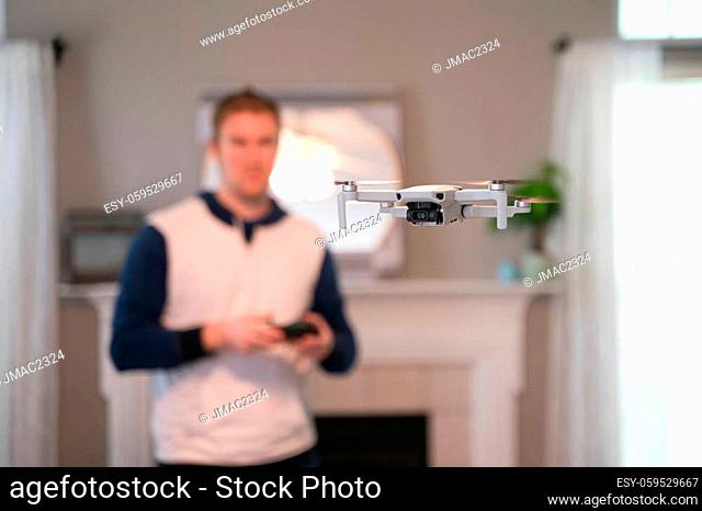 Drone flying indoors with pilot visible in background. Amateur drone flight. User wearing sweatshirt flying drone inside of home on cold day