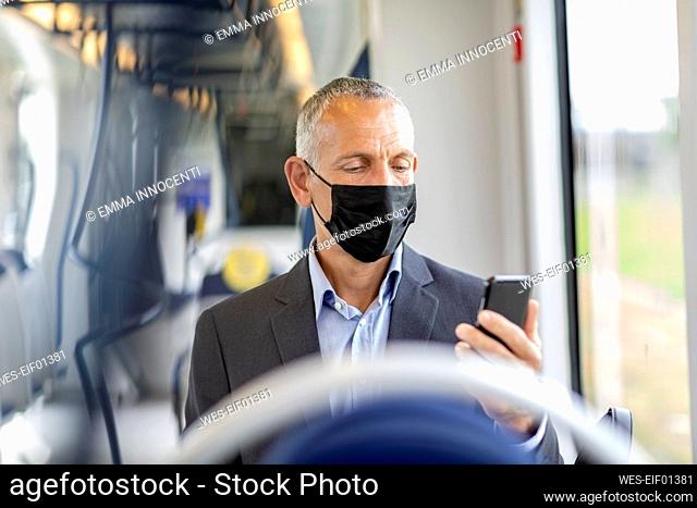 Businessman using smart phone in tram during COVID-19