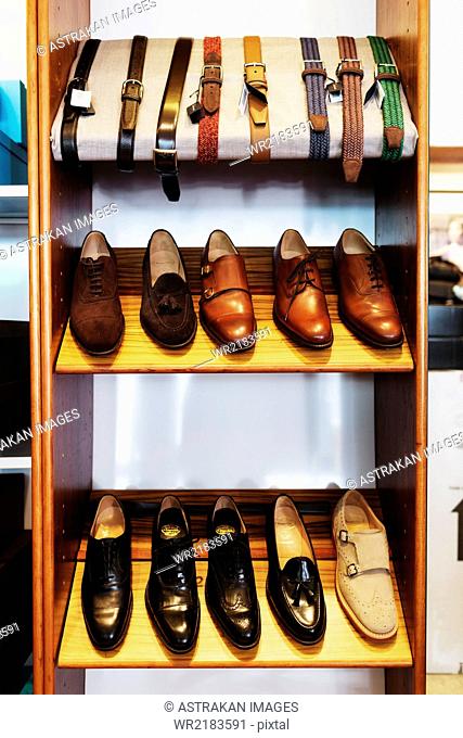 Leather shoes and belts arranged on shelves at clothing store