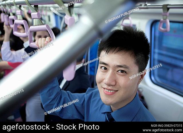 Portrait of smiling young businessman standing on the subway, looking at camera