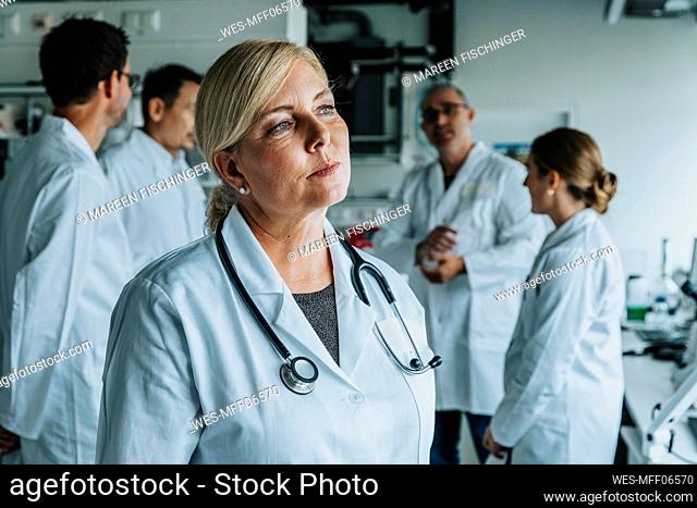 Female scientist looking away while standing with coworker in background at laboratory