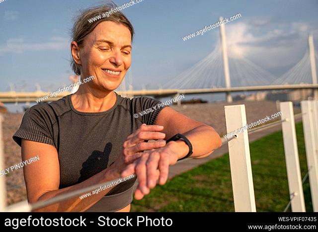 Smiling mature woman checking time in smart watch at railing