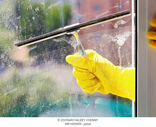hand in yellow glove cleans window by squeegee