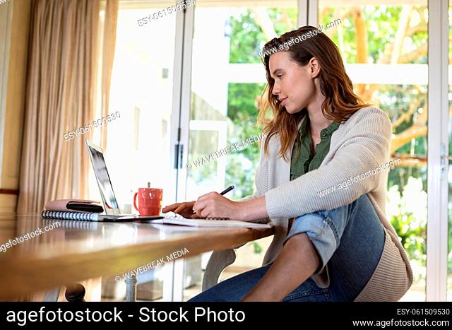 Woman taking notes while using laptop at home