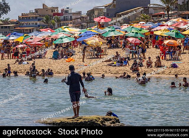15 November 2023, Brazil, Salvador: People bathe in the middle of the week and sit under umbrellas on Arembepe beach during a heatwave