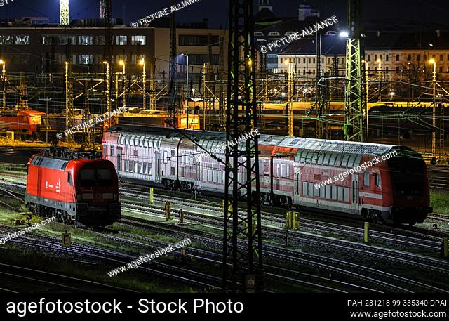 18 December 2023, Saxony, Leipzig: A suburban train and an electric locomotive stand on sidings at Leipzig Central Station in the early morning