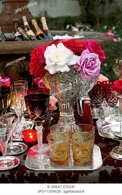 Various cut glasses and a bunch of flowers on a table at a garden party