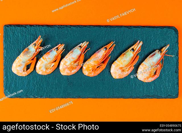 Traditional fried black tiger prawn stand on a slate board which stands on an orange background. Top views