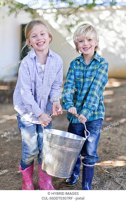 Children carrying heavy pail outdoors