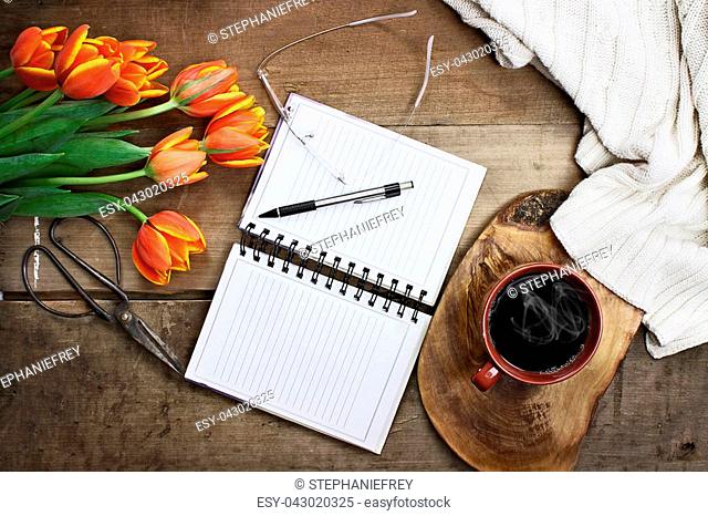 Overhead shot a bouquet of an open book or garden planner, glasses, coffee, sissors and flowers over a wood table top ready to plan an agenda