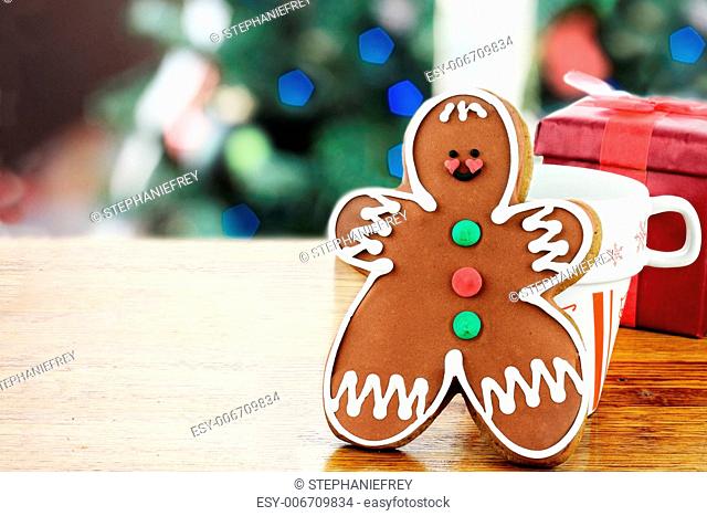 Gingerbread man cookie has been set out for Santa with a cup of milk. Christmas tree in the background