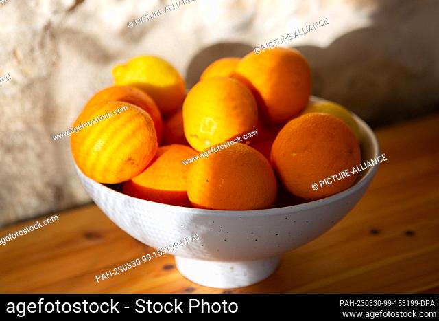 26 March 2023, Portugal, Tomar: Oranges and lemons lie in a bowl that stands on a sideboard in front of a stone wall. Photo: Viola Lopes/dpa