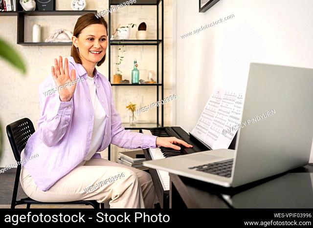 Smiling woman waving during video call on laptop at home