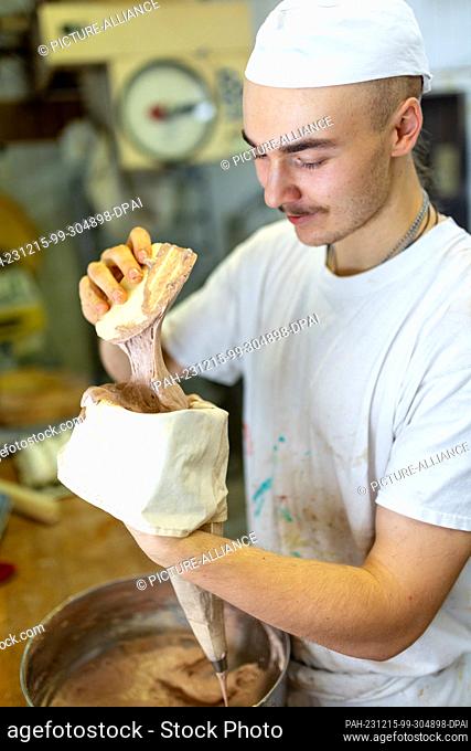 PRODUCTION - 13 December 2023, Thuringia, Erfurt: Baker Louis Braun puts dough into a piping nozzle at the Lobenstein bakery and patisserie
