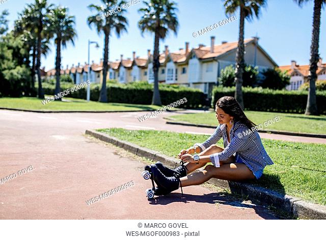 Spain, Gijon, teenage girl sitting on curb tying her roller skates