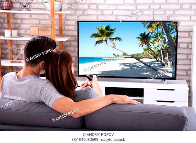 Young Couple Sitting On Sofa Watching Television At Home