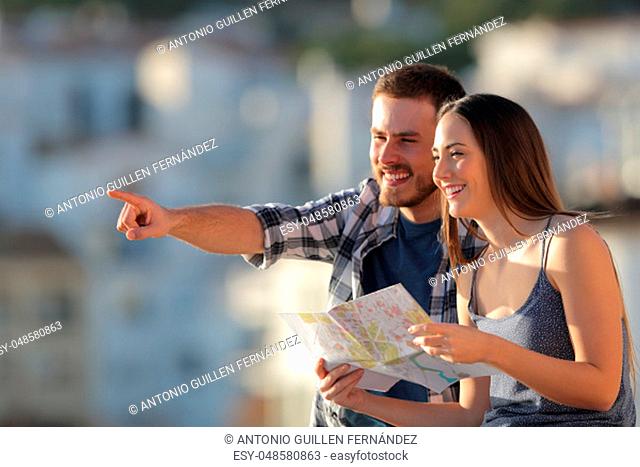 Happy couple of tourists holding paper map pointing away in a town on vacation