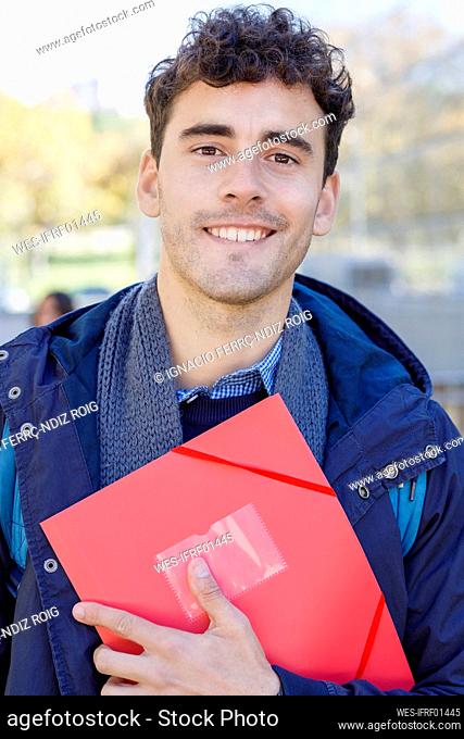 Smiling man with red file at campus