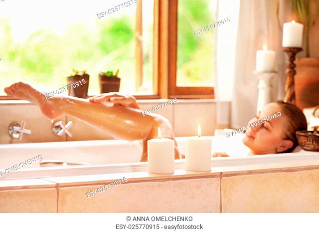 Soft focus photo of gentle young woman lying down in bath tub with foam and candle, enjoying spa procedure in the luxury resort
